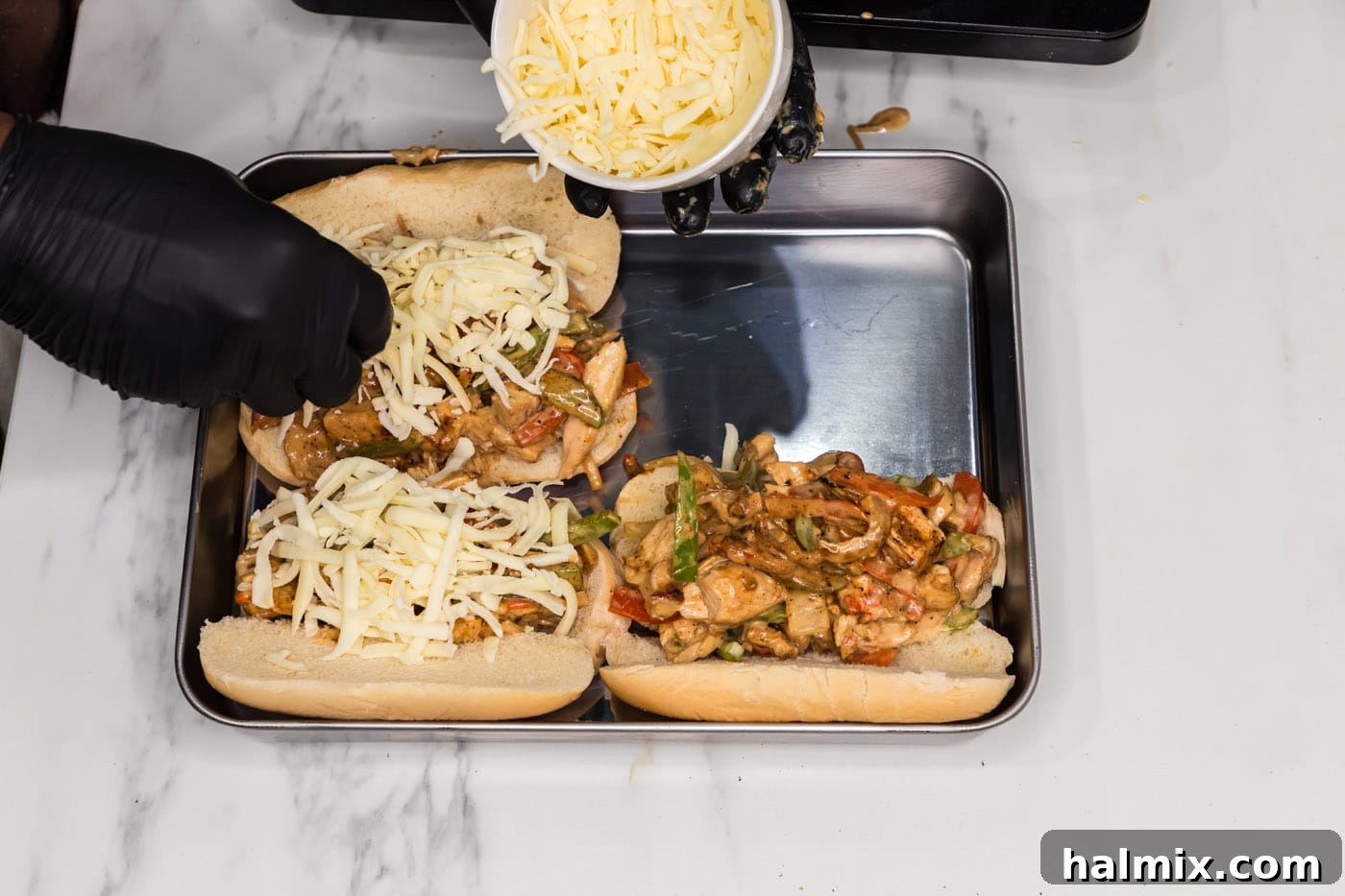 sprinkling mozzarella cheese over chicken philly cheesesteak sandwiches