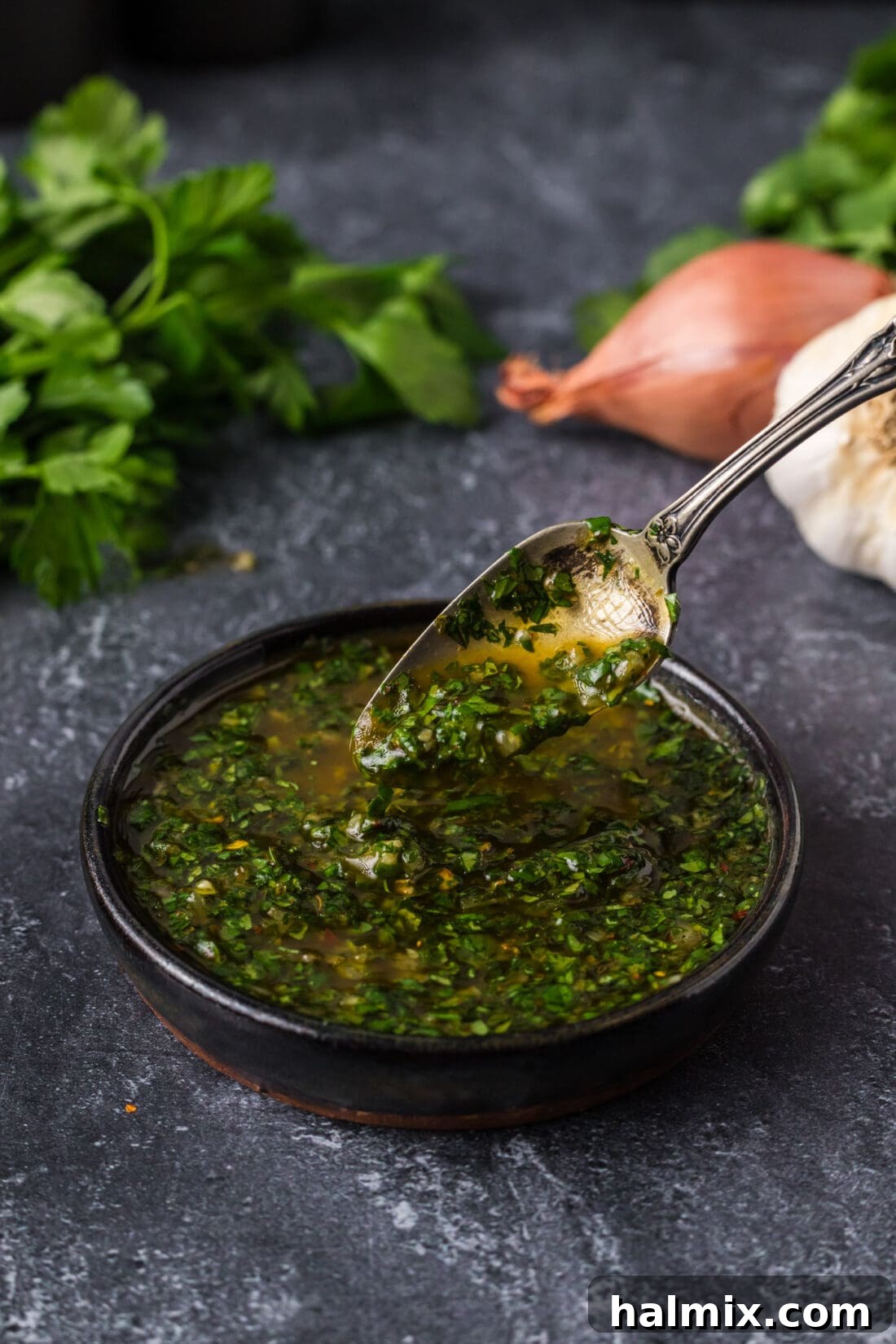 Drizzling Fresh Chimichurri A spoon drizzling homemade chimichurri sauce into a bowl of chimichurri, showcasing its rich texture.
