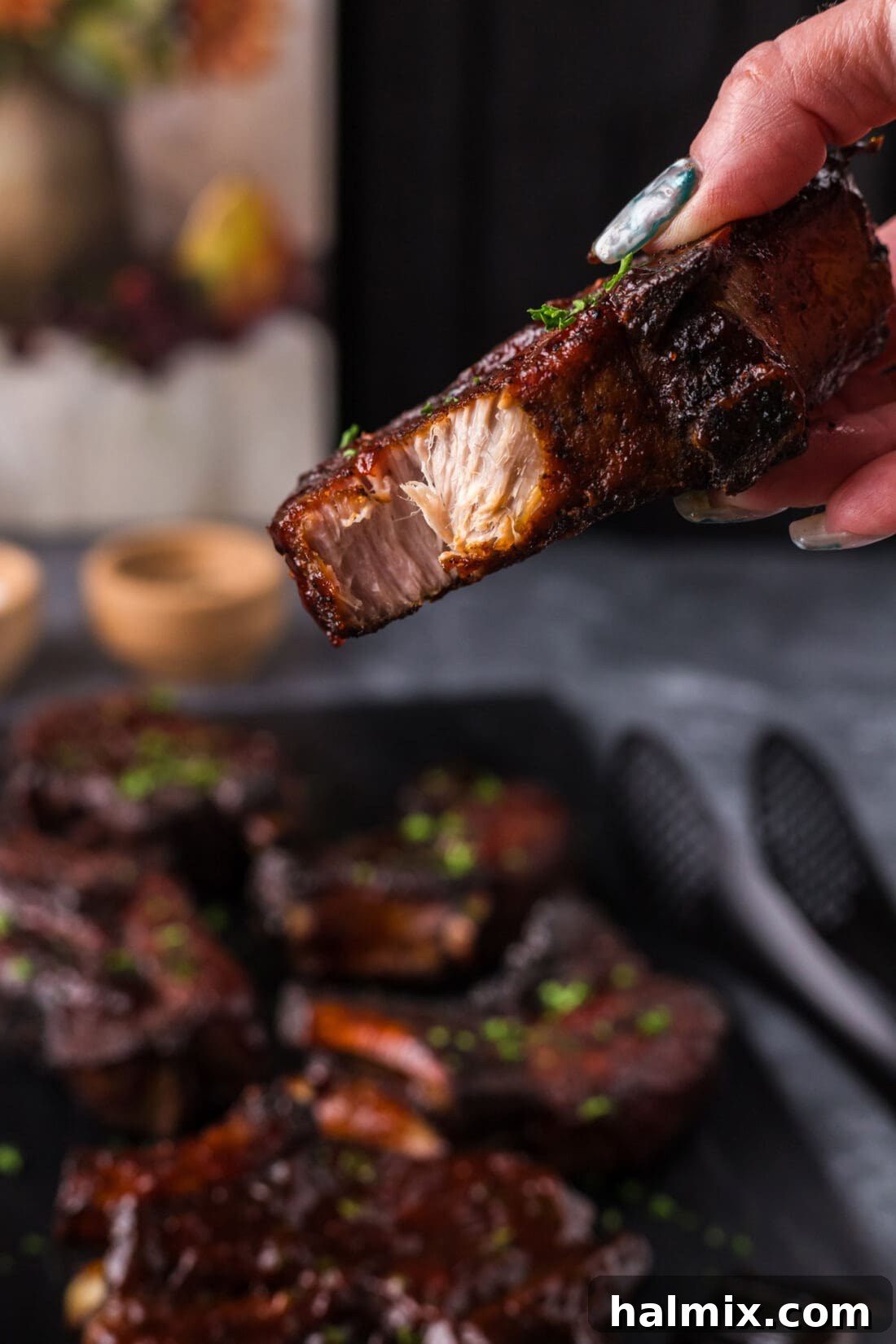 A hand holding a succulent Country Style Rib with a bite taken out, highlighting its tenderness and juicy interior.