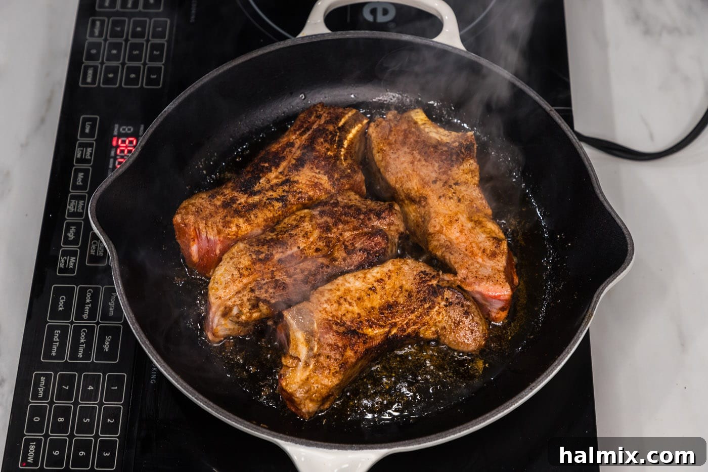 Seared pork ribs browning beautifully in a skillet before oven baking.