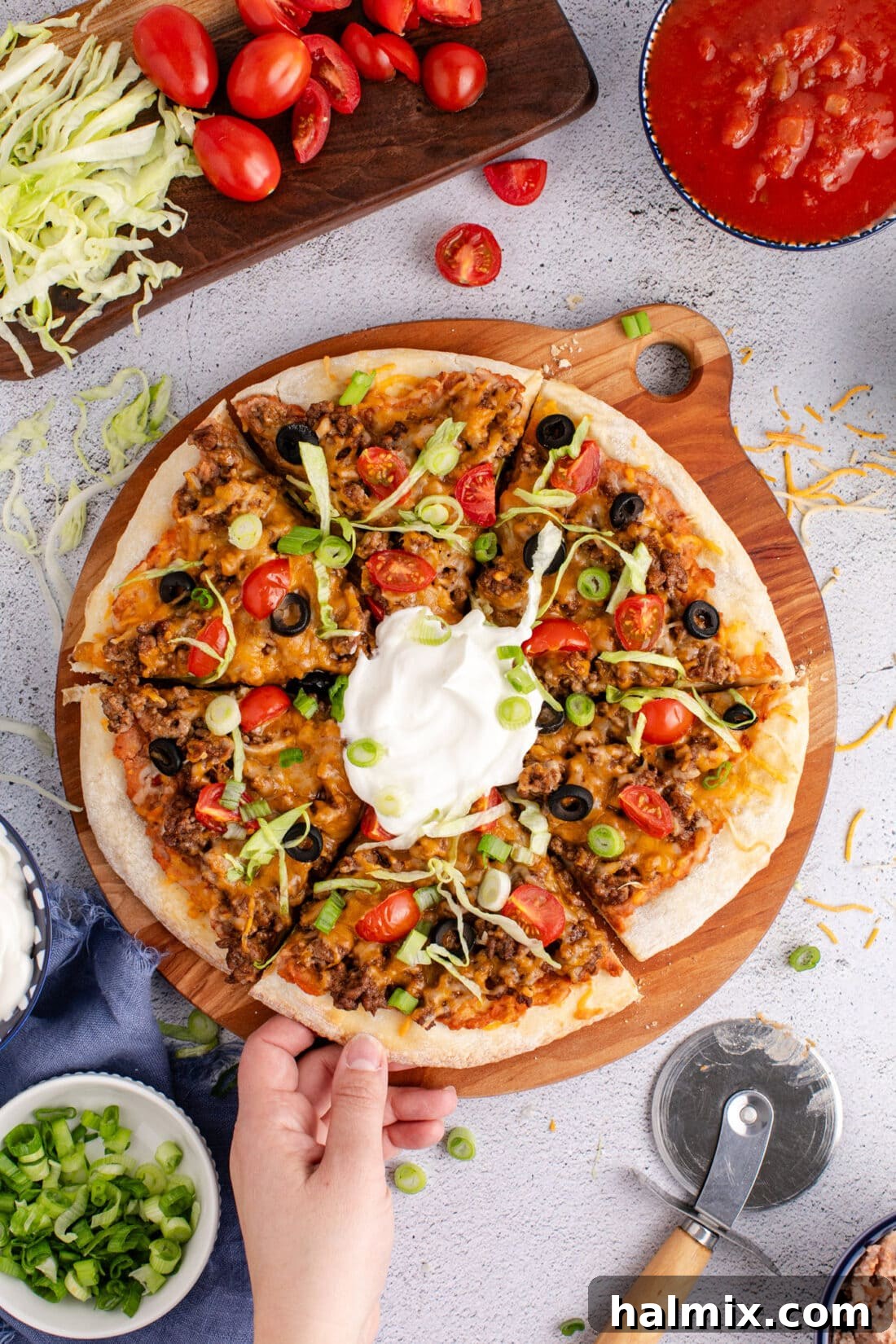 Hand grabbing a slice of Taco Pizza from a serving board