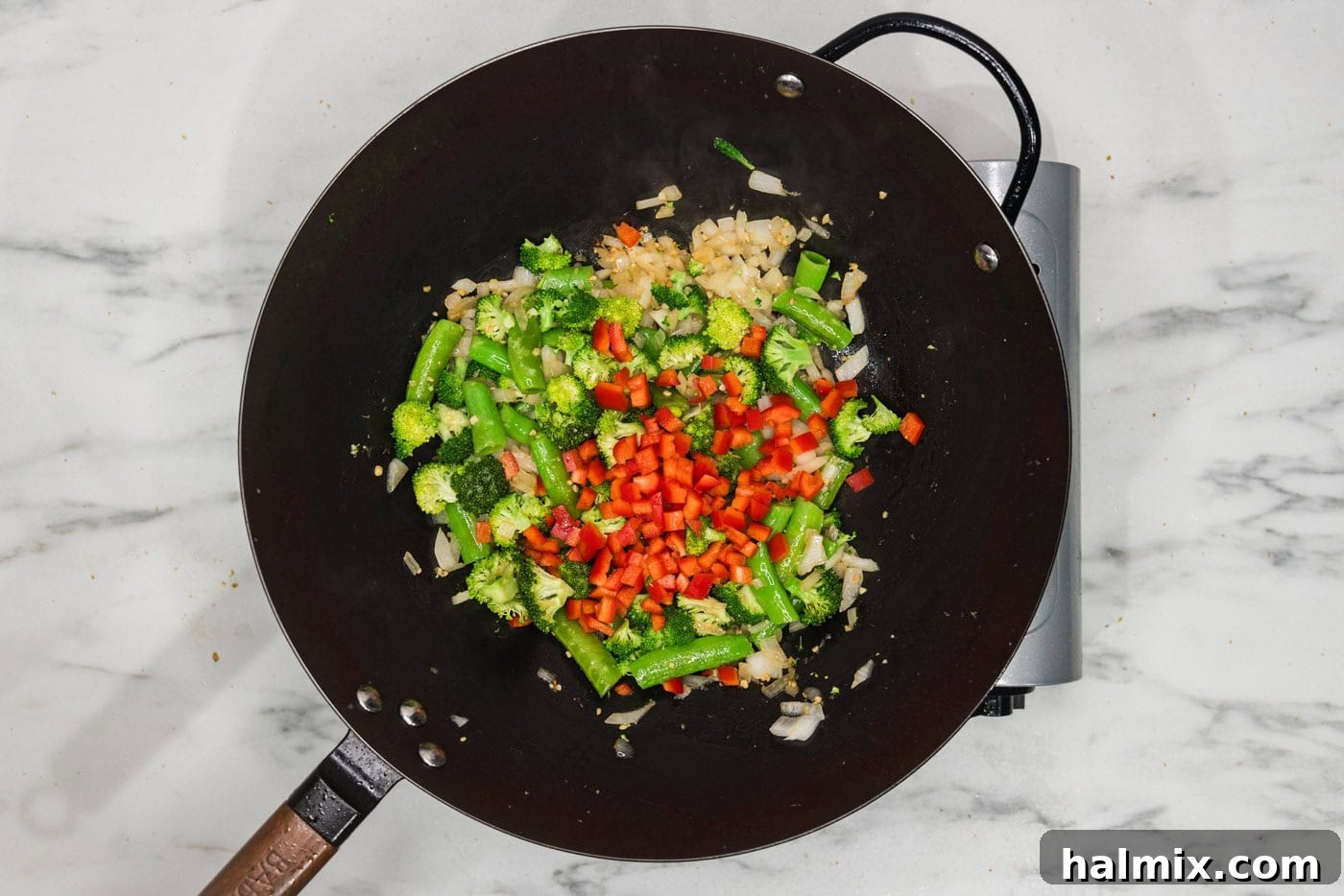 Onion, snap peas, broccoli, and red bell pepper in a wok