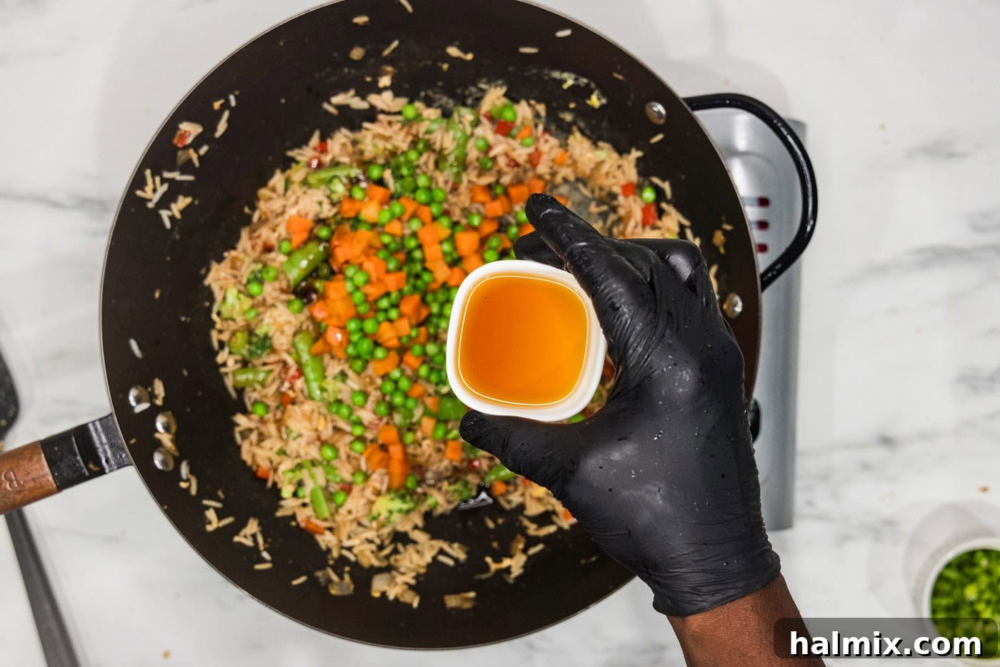 sesame oil in a bowl held over a wok of vegetable fried rice