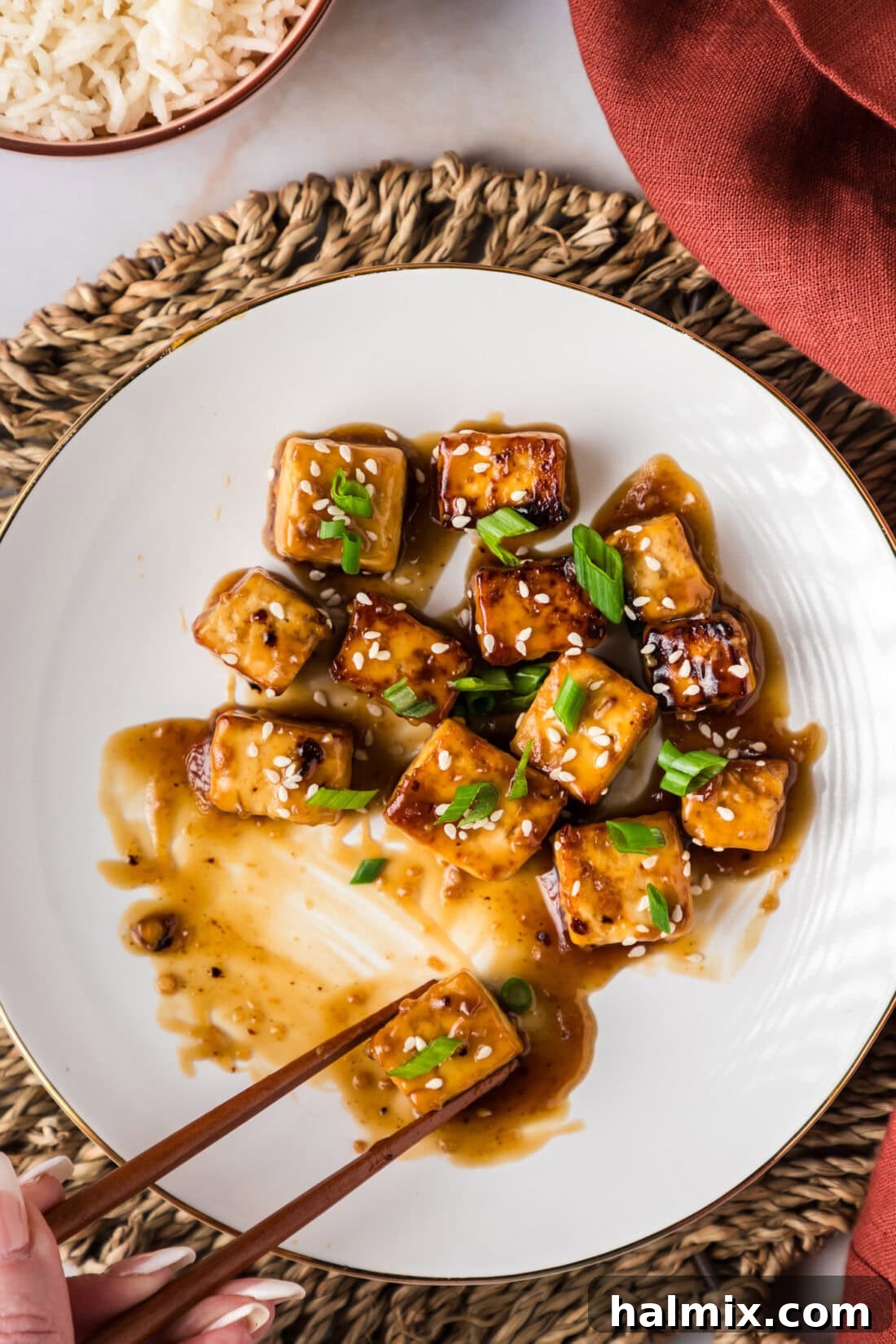 Sticky Honey Garlic Tofu 3 Chopsticks grabbing a piece of Honey Garlic Tofu on a plate, highlighting its appetizing glaze.