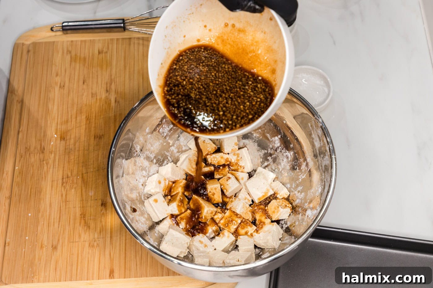 Sticky Honey Garlic Tofu 8 Pouring a portion of the honey garlic sauce over cornstarch-coated tofu cubes for initial flavoring.