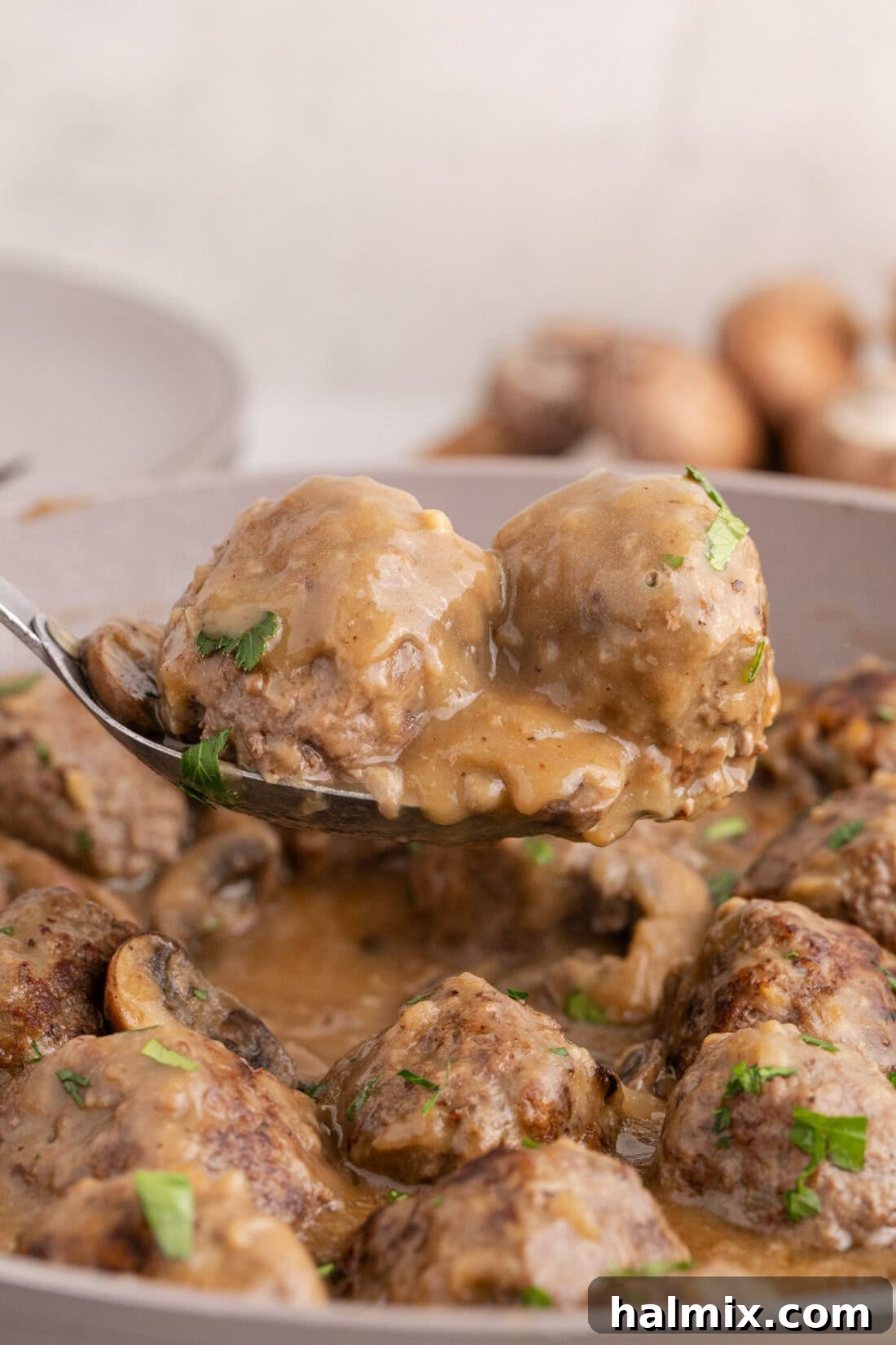 Two Salisbury Steak Meatballs on a spoon held above a skillet of Salisbury Steak Meatballs, ready to be served over mashed potatoes.