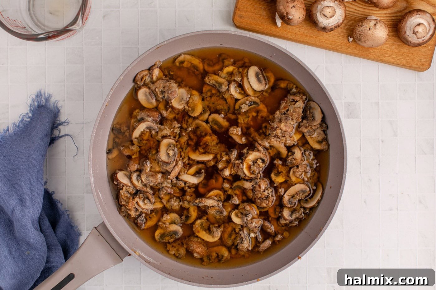 Beef broth and Worcestershire sauce being poured into the mushroom sauce in the skillet