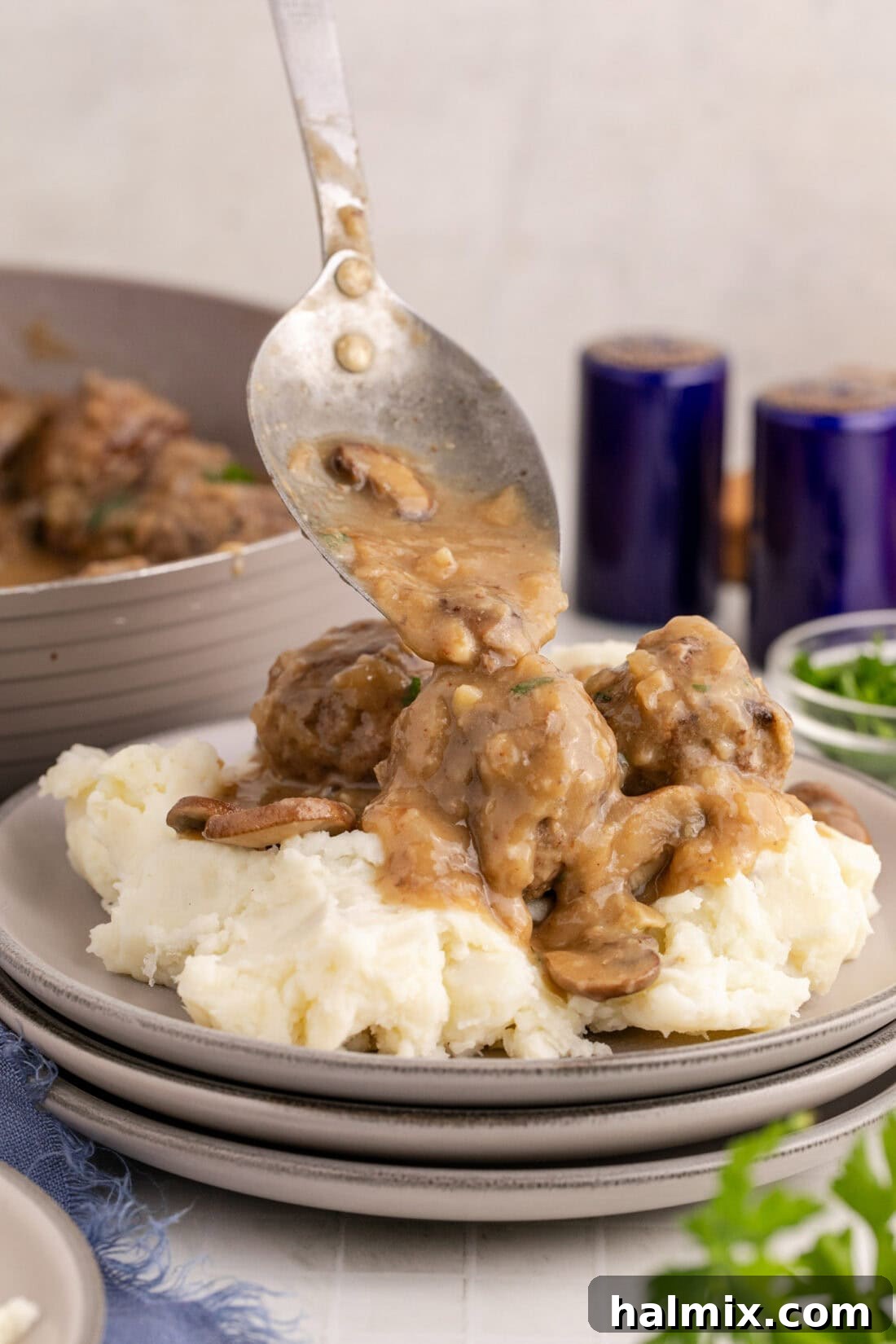 Gravy being generously spooned over Salisbury Steak Meatballs and fluffy mashed potatoes, highlighting the rich texture of the sauce.