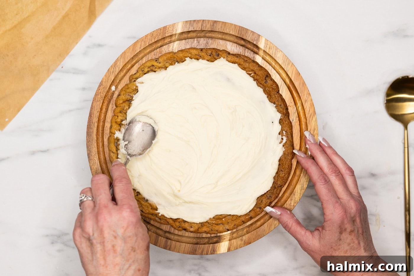 spreading buttercream frosting overtop a jumbo chocolate chip cookie