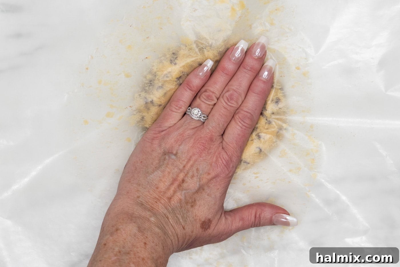 hand flattening cookie dough ball with wax paper