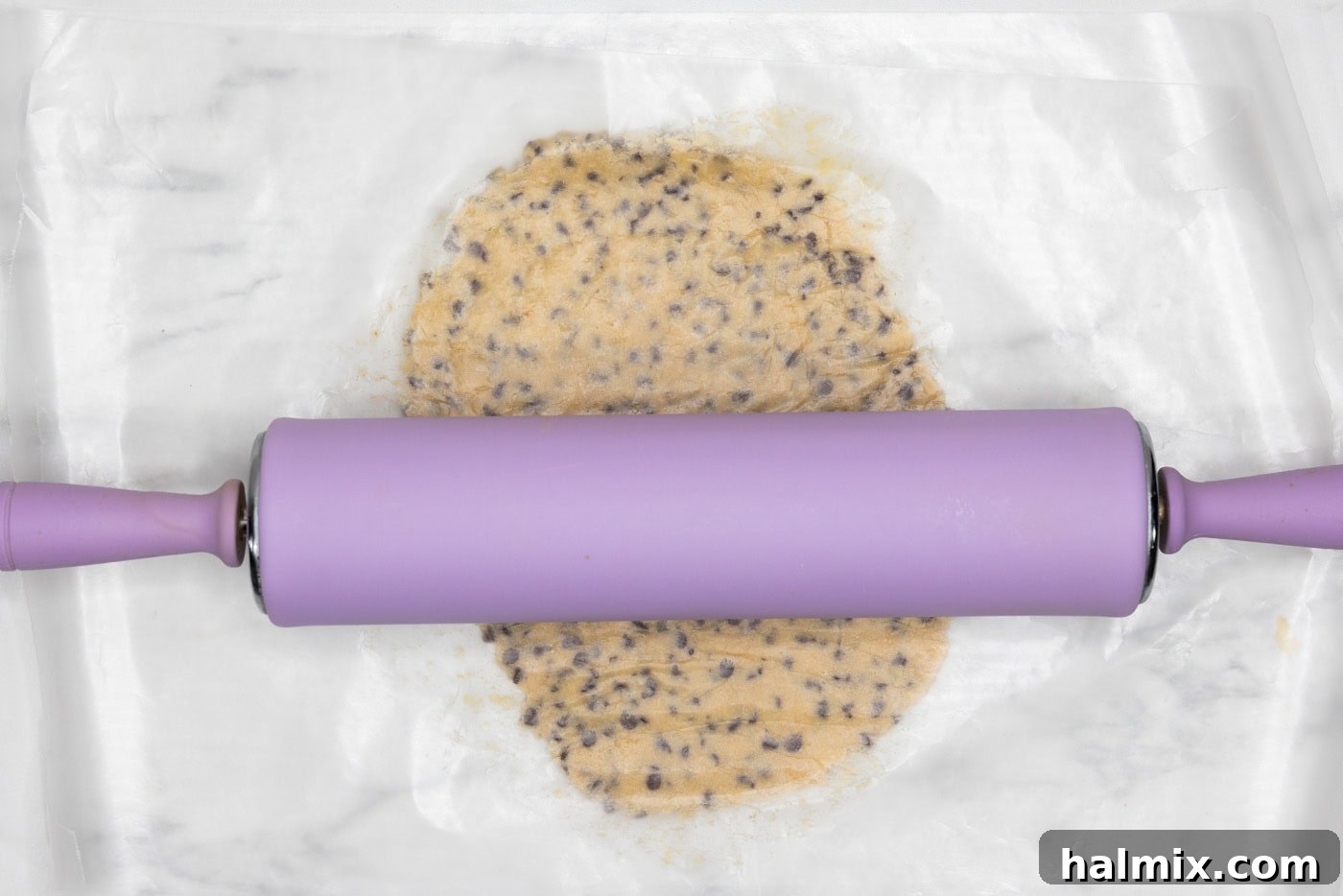 rolling pin flattening cookie dough ball between parchment paper