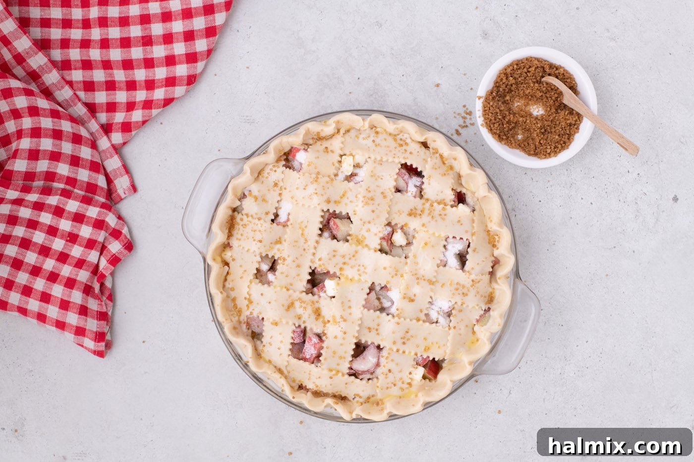 Tangy Rhubarb Delight 19 Turbinado sugar being sprinkled generously over the egg-washed lattice top of a rhubarb pie.