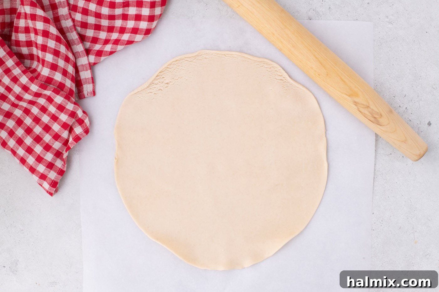 Tangy Rhubarb Delight 5 Pie dough being rolled out on a parchment-lined surface with a rolling pin.