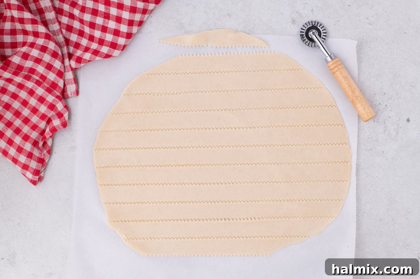 Tangy Rhubarb Delight 10 Pie dough being cut into even strips using a pastry cutter on a parchment-lined surface.