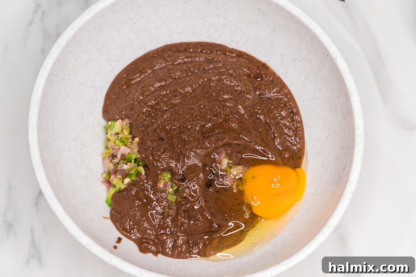 blended black bean mixture added to bowl with an egg, sauteed veggies, and whole black beans
