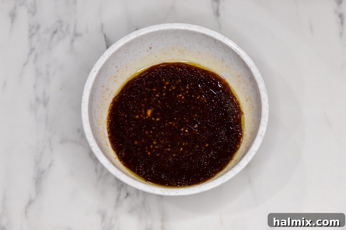 Sweet and Sticky Instant Pot Bourbon Chicken 5 A close-up view of the bourbon chicken sauce being whisked in a glass bowl, showcasing its rich, dark color and smooth consistency.