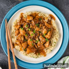 Close up photo of a plate of Instant Pot Bourbon Chicken garnished with green onions and sesame seeds, showcasing the rich, sticky sauce and tender chicken.