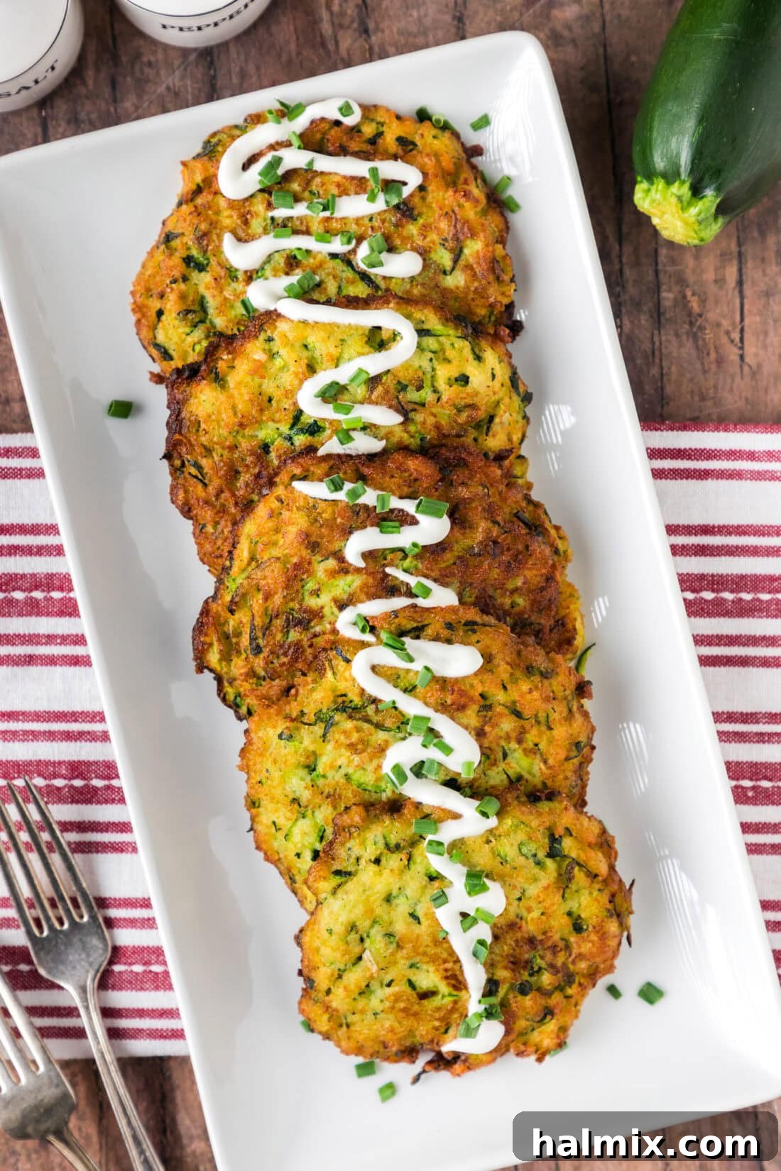 Golden Zucchini Delights 3 Zucchini Fritters arranged on a platter with a light drizzle of sour cream and fresh herbs