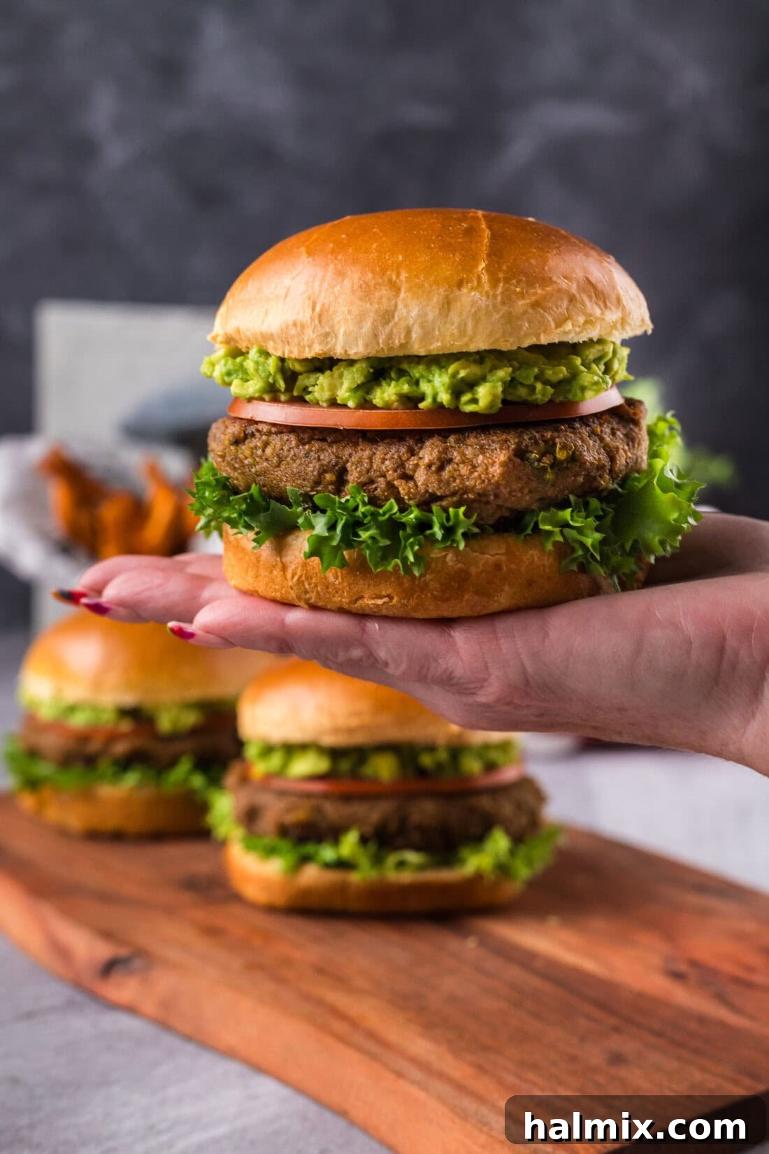 Hand holding up a Veggie Burger with two more on a platter in the background
