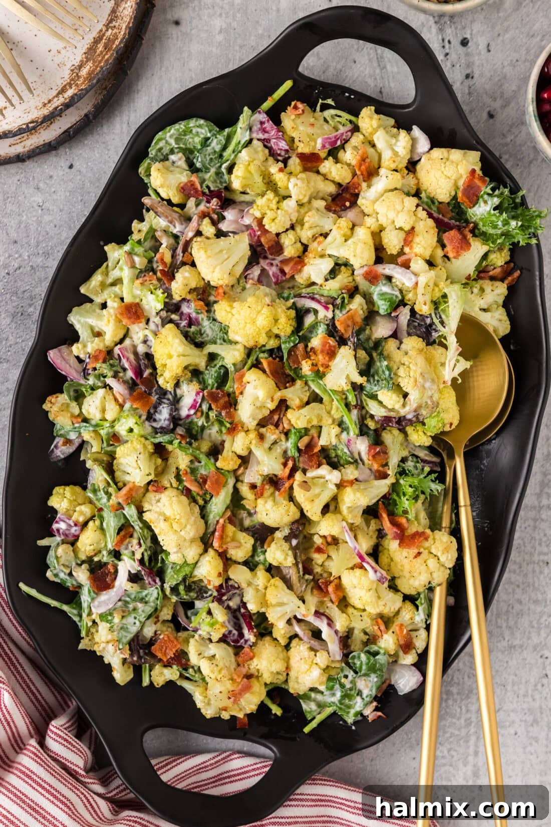 Cauliflower Salad on a black platter with two serving spoons, ready to be served at a potluck or cookout.