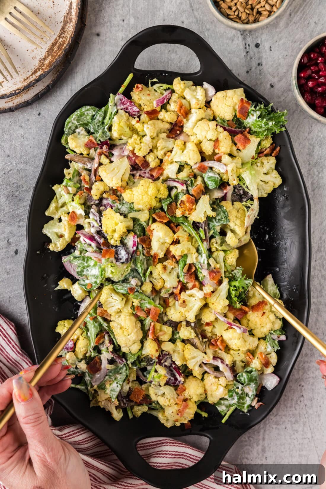 Hands picking up Cauliflower Salad using serving spoons, ready to be dished out.