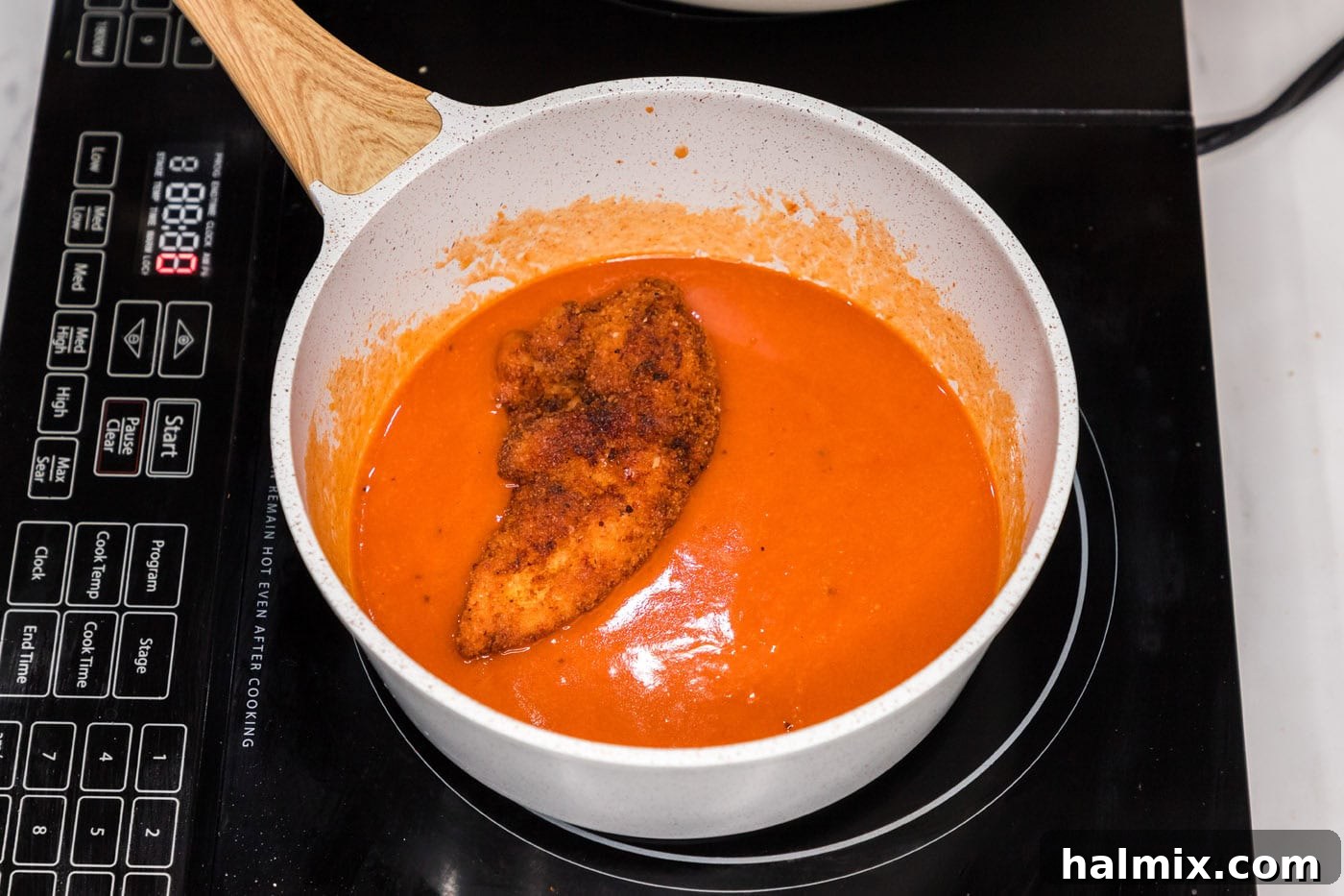 fried chicken tender dipped into buffalo sauce in a pan