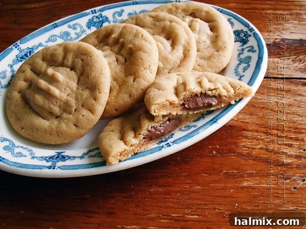 Melting Chocolate Core Peanut Butter Cookies 4 A trio of freshly baked chocolate stuffed peanut butter cookies on a serving plate, with one cookie expertly broken to reveal the soft, melted Hershey's chocolate within. The image highlights the tempting texture of these homemade sweets.