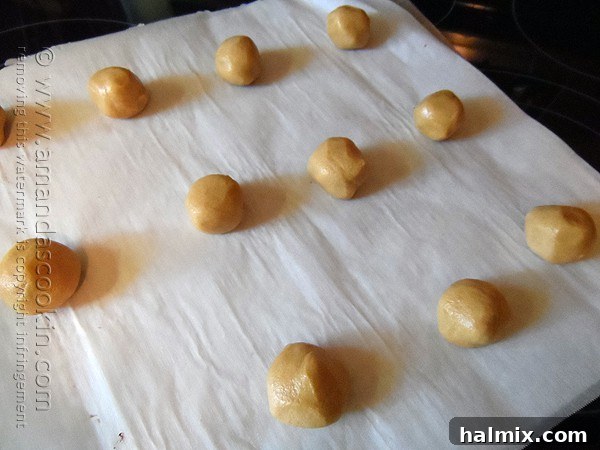 Melting Chocolate Core Peanut Butter Cookies 7 Rows of precisely formed chocolate stuffed peanut butter cookie dough balls, each with the characteristic criss-cross pattern, arranged on a parchment-lined baking sheet, ready for the oven.