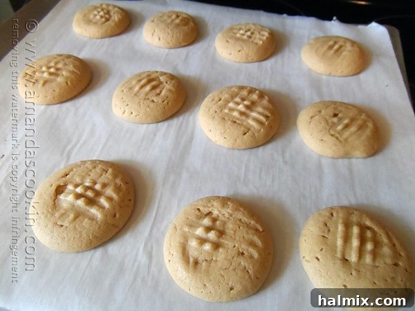 Melting Chocolate Core Peanut Butter Cookies 8 A batch of golden-brown chocolate filled peanut butter cookies, freshly baked and adorned with their classic criss-cross pattern, cooling on parchment paper on a baking sheet.