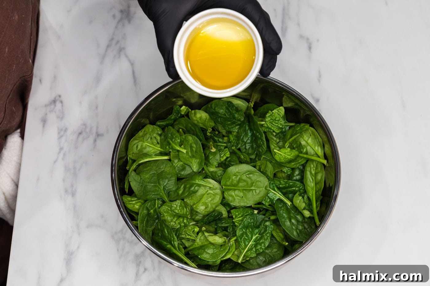 Pouring olive oil over fresh spinach leaves in a large mixing bowl.