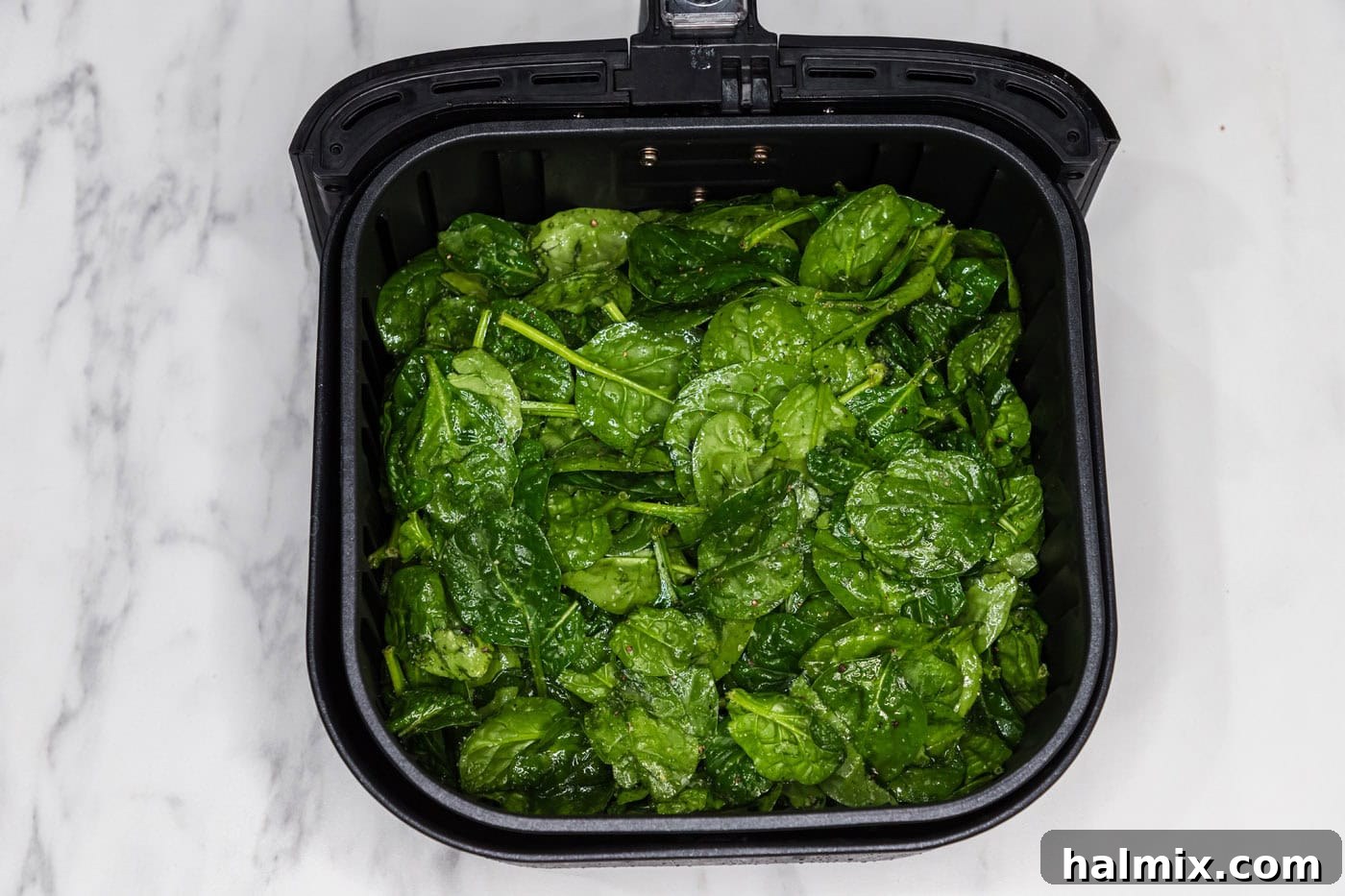 Seasoned spinach leaves placed inside an air fryer basket, ready for cooking.