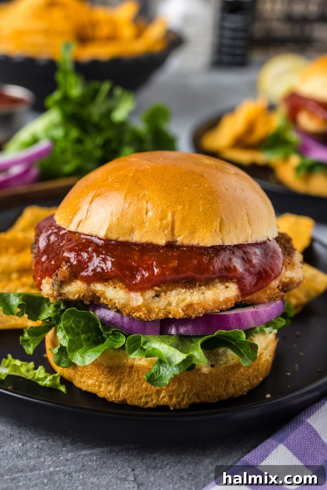 Two golden-brown shrimp burgers served on buns, one in the foreground with a clear view of its crispy exterior, and another slightly blurred in the background.