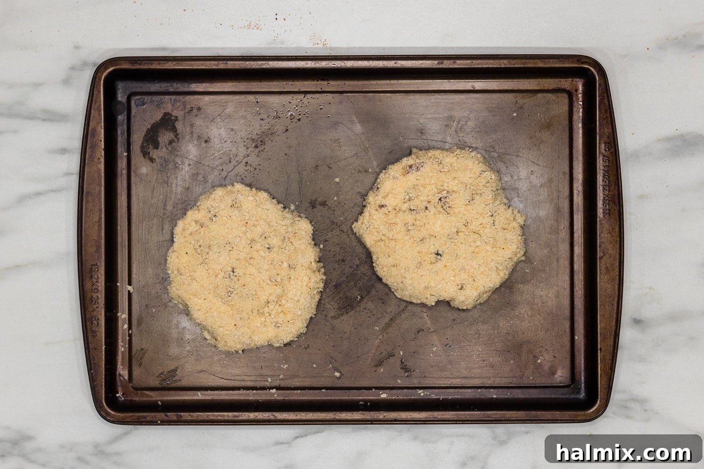 Three perfectly breaded shrimp burger patties resting on a baking sheet, ready for frying.