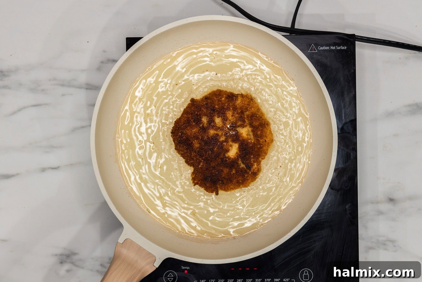A shrimp burger patty frying to a perfect golden brown in a hot skillet of oil.