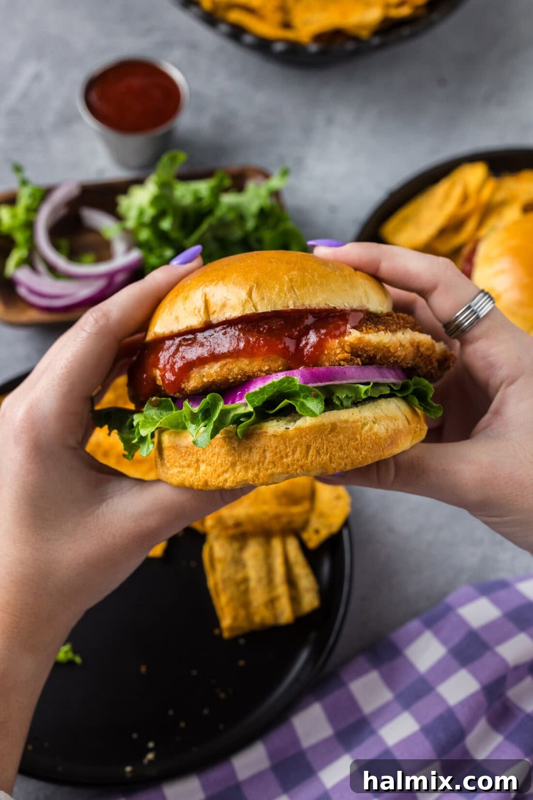 Hands holding up a Shrimp Burger with a soft bun and fresh toppings.