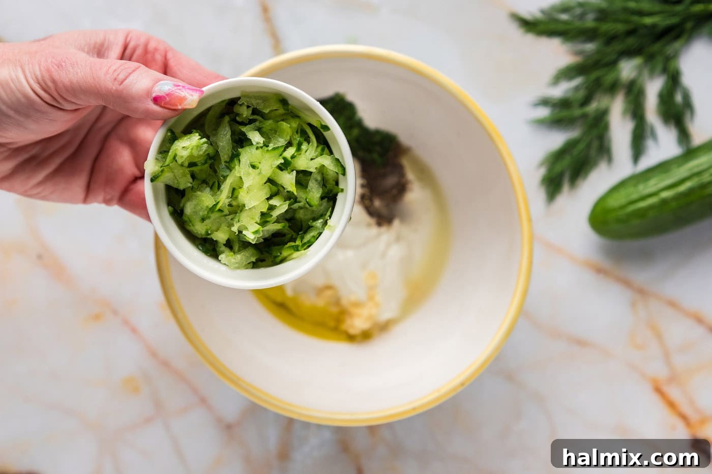 Adding squeezed, shredded cucumber to a bowl of creamy Greek yogurt, fresh dill, minced garlic, and other essential Tzatziki ingredients, ready for gentle mixing.