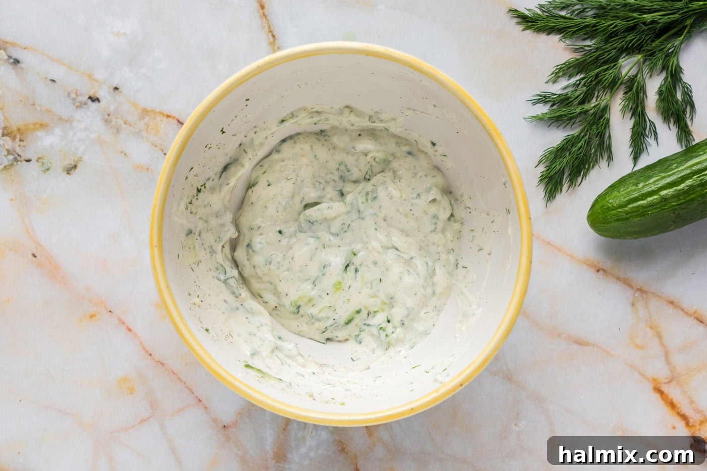 A mixing bowl filled with freshly combined Tzatziki Sauce, showing its creamy consistency and flecks of green dill, chilling in the refrigerator to allow flavors to meld.
