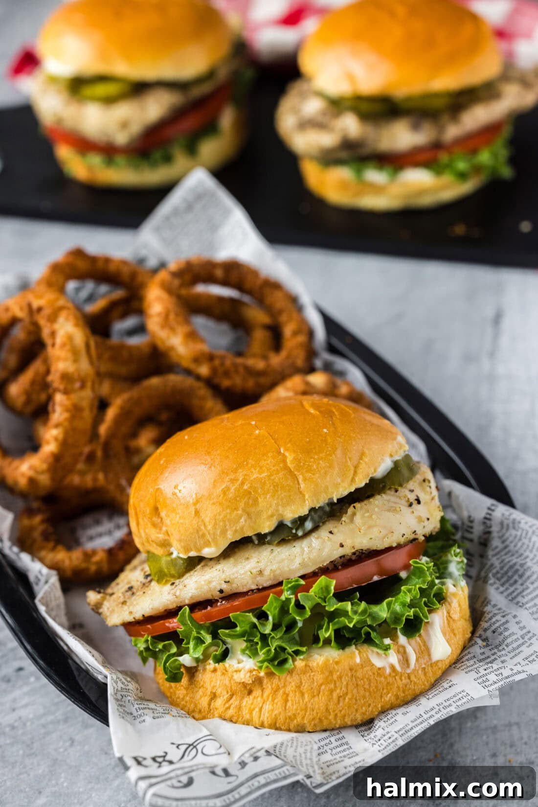 Juicy grilled chicken sandwich in a basket with crispy onion rings on the side