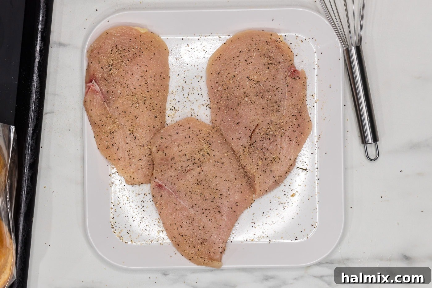 Seasoned chicken breasts on a plate, ready for grilling