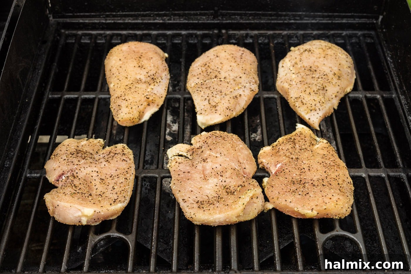 Seasoned chicken breasts cooking on a hot grill, showing early grill marks