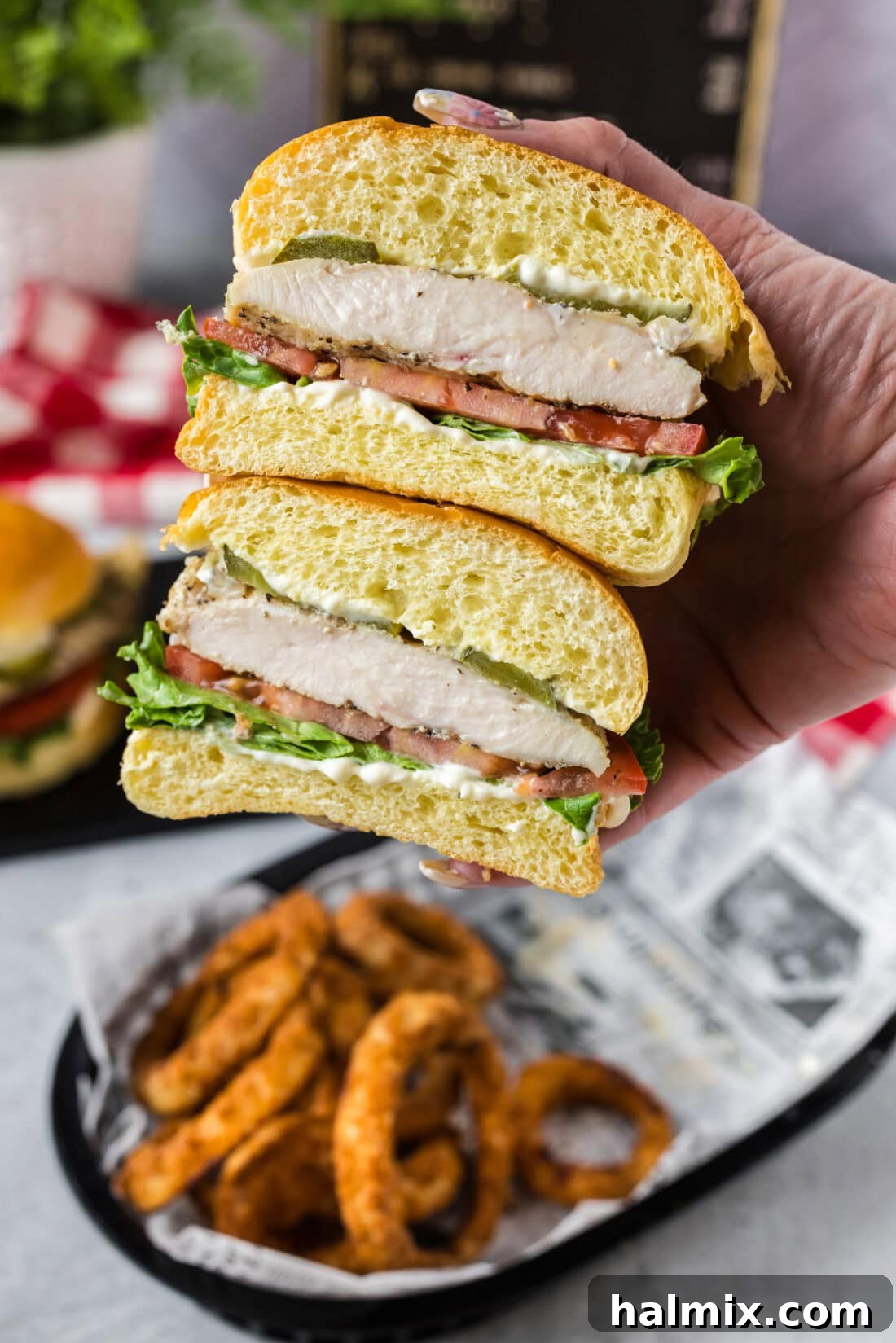Hand holding a grilled chicken sandwich cut in half, showcasing the layers of chicken and fresh toppings