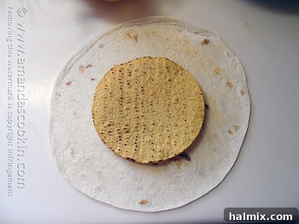 A crispy tostada shell being placed gently on top of the seasoned ground beef and nacho cheese layers on a flour tortilla, forming the core of the Crunchwrap Supreme.