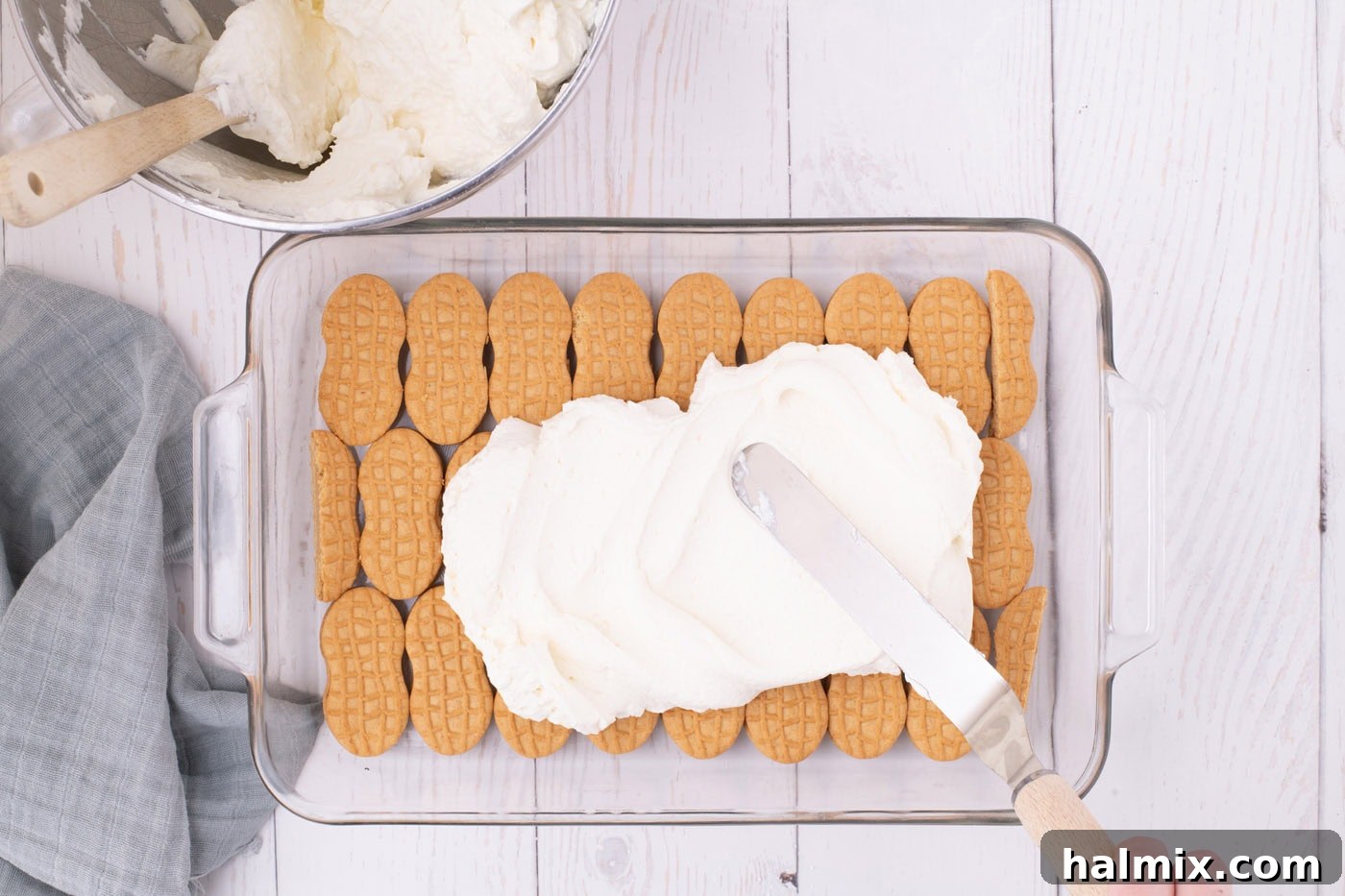 Nutter Butter Dream Cake 7 spreading whipped cream cheese layer over nutter butter cookies with an offset spatula