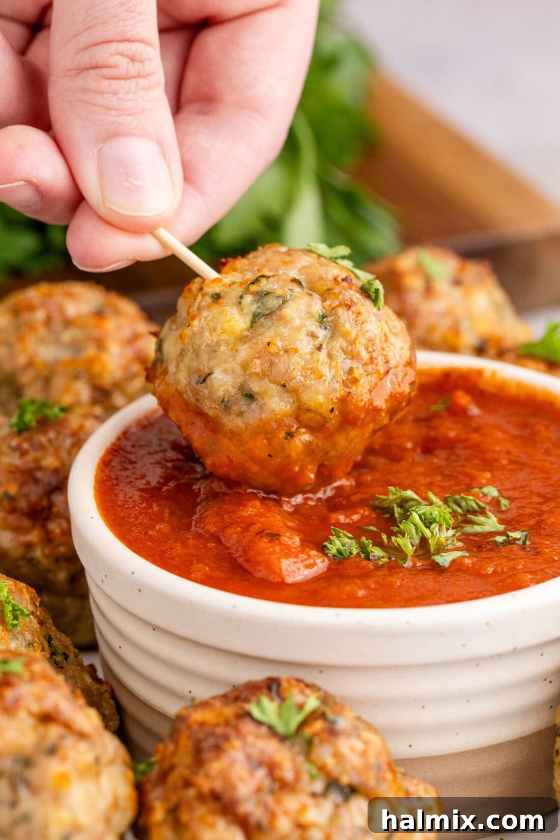 A baked chicken meatball being dipped into a bowl of bright red marinara sauce.