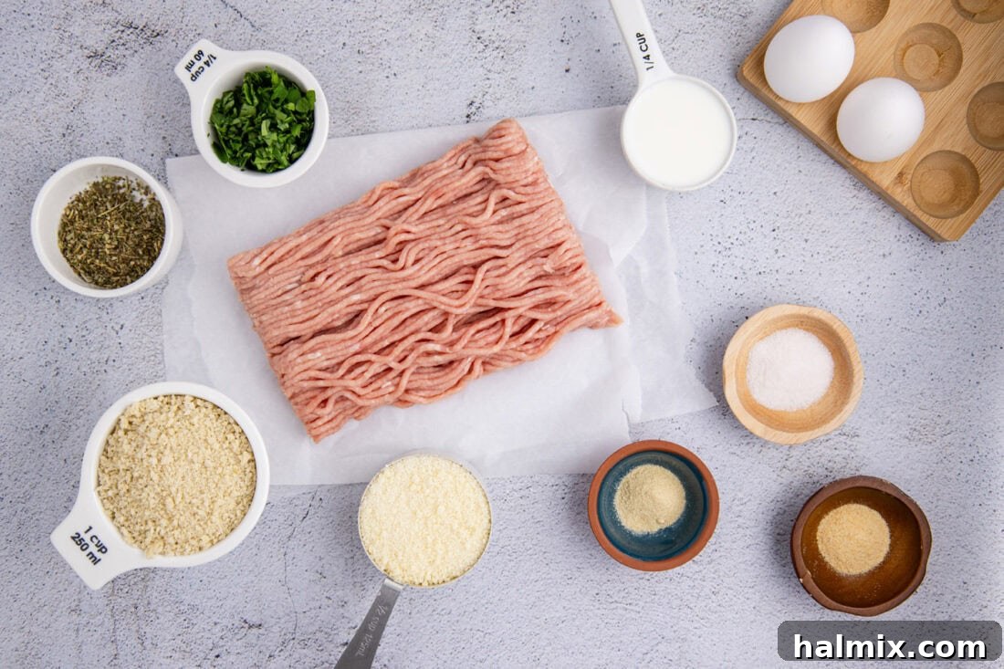 A collection of ingredients laid out on a counter, including ground chicken, panko breadcrumbs, parmesan cheese, parsley, milk, and various seasonings.