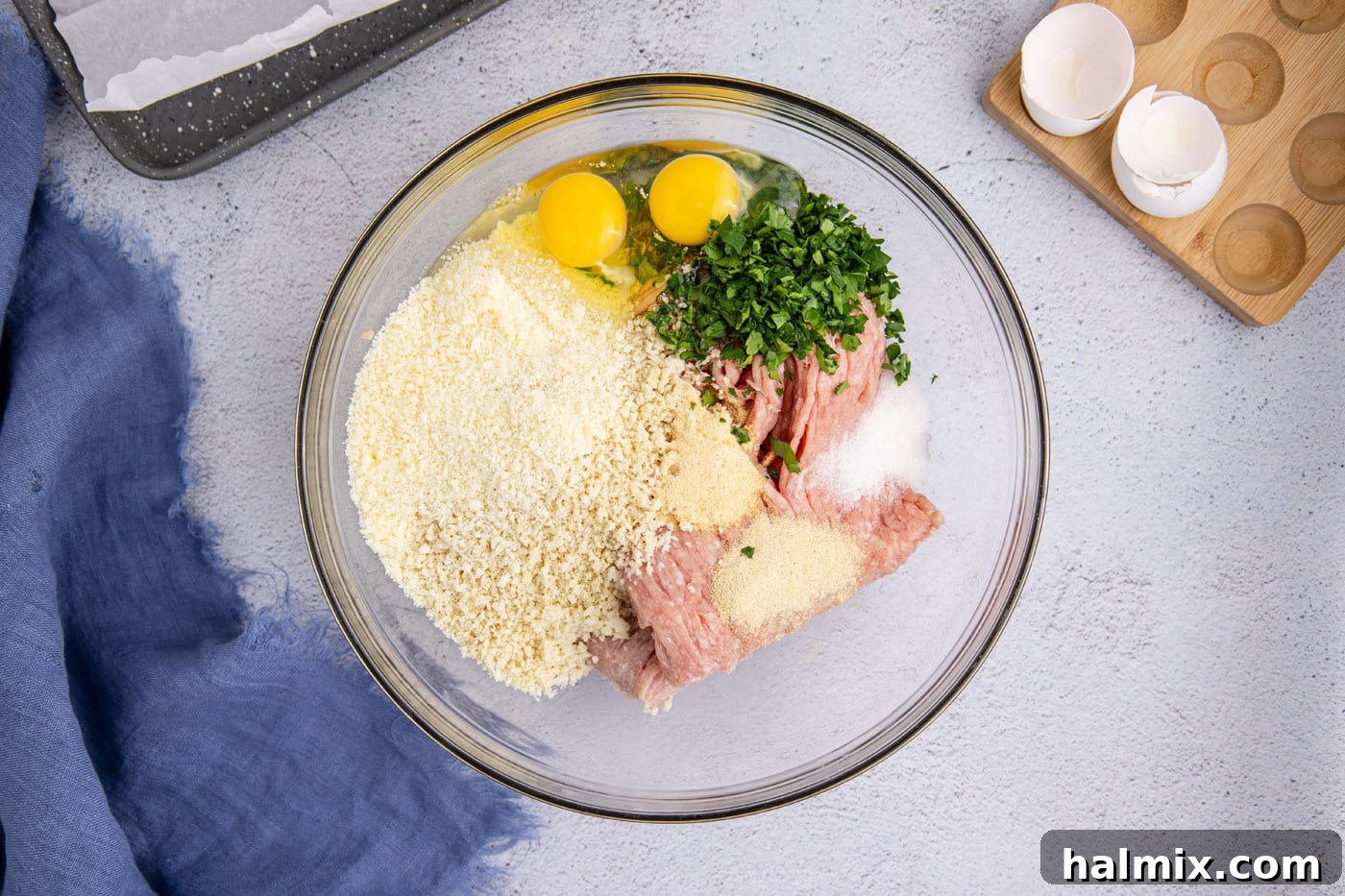 Ground chicken in a bowl with egg, panko breadcrumbs, parsley, milk, and various seasonings, ready to be mixed.