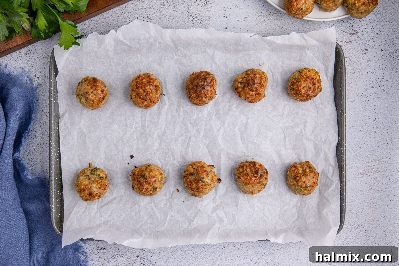 Freshly baked, golden-brown chicken meatballs resting on parchment paper on a baking sheet.