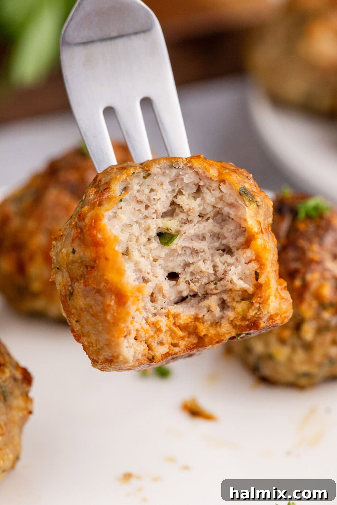 A baked chicken meatball on a fork, with a small bite taken out, showing its tender interior.