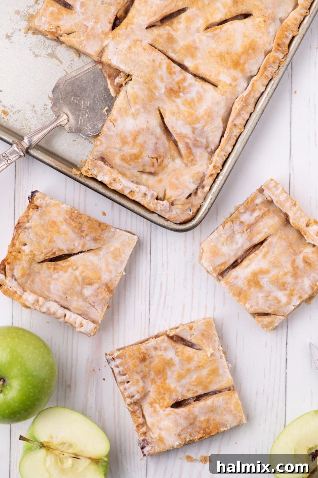 Three generous slices of warm Apple Slab Pie, showcasing its golden crust and delicious apple filling, resting on a rustic wooden table with the full baking pan blurred in the background, ready for a large gathering.