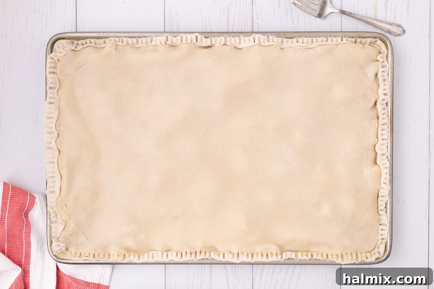 The completed apple slab pie with both top and bottom crusts sealed and crimped around the edges, ready for baking.